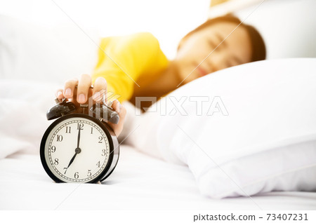 Young asian woman wake up early in morning. She lying on bed and trying turn off alarm clock 73407231