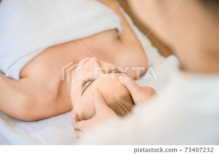 Beautiful woman receiving head and facial massage in spa salon Beautiful woman receiving head and facial massage in spa salon 73407232