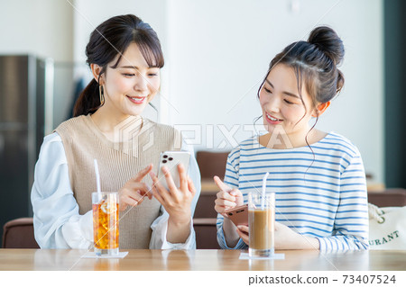 一個年輕的女人,看著一家咖啡館的智能手機 一個年輕的女人,看著一家咖啡館的智能手機 73407524