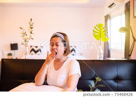 Woman yawning during sitting on sofa and tired sleepy,Female with symptoms sleepiness 73408426