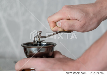 mechanical machine for grinding coffee beans in the hands of a person 73409782