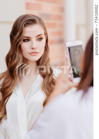 A beautiful woman in white clothes is photographed on phone for social networks. A beautiful woman in white clothes is photographed on phone for social networks. 73410082