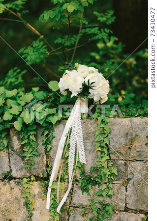 bridal bouquet of peonies with white ribbons on the brick wall 73410477
