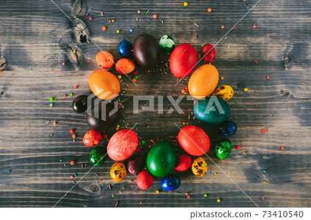 A ring of Easter eggs on a wooden background. A circle of colorful eggs and decorative sugar powder. Easter backgrounds 73410540
