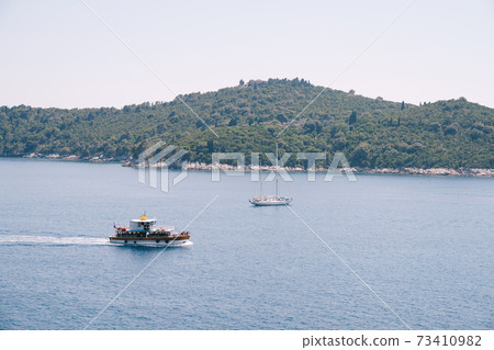 Lokrum is a small island in the Adriatic Sea, near Dubrovnik, Croatia. Tourist ships sail past the island, a sailing yacht moored near the coast. Lokrum is a small island in the Adriatic Sea, near Dubrovnik, Croatia. Tourist ships sail past the island, a sailing yacht moored near the coast. 73410982