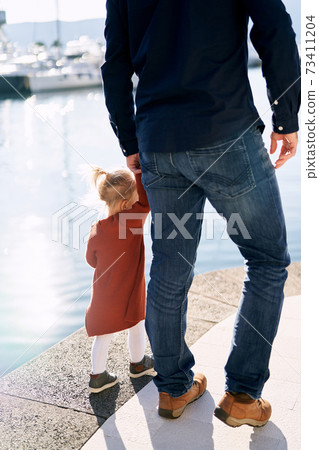 Father and daughter are walking hand in hand by the sea on a sunny day Father and daughter are walking hand in hand by the sea on a sunny day 73411204