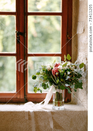 bridal bouquet of white peonies, roses, pink protea, snowberry, branches of eucalypt tree and white ribbons on the window bridal bouquet of white peonies, roses, pink protea, snowberry, branches of eucalypt tree and white ribbons on the window 73411205