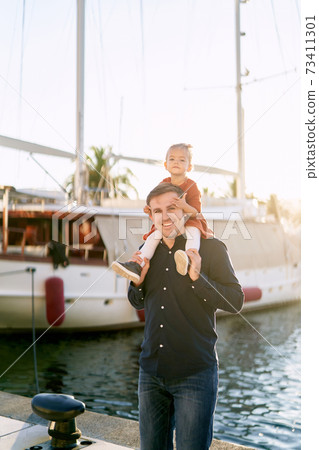 Little girl is sitting on her daddy's shoulders on a boat pier in Porto Montenegro Little girl is sitting on her daddy's shoulders on a boat pier in Porto Montenegro 73411301