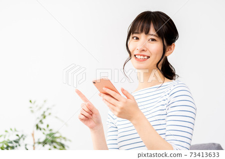 A woman who operates a smartphone while relaxing in the living room. 73413633