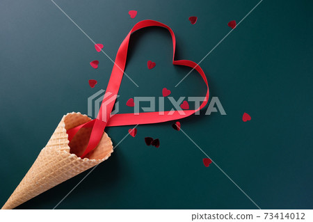 Waffle cone with red ribbon in the shape of heart 73414012