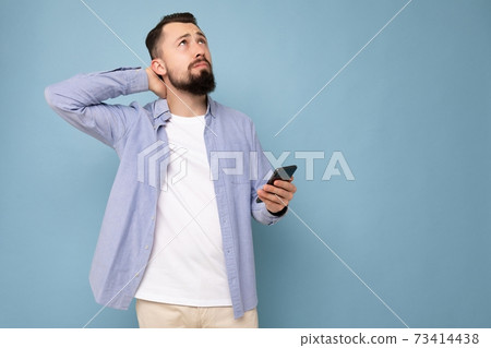 Thoughtful handsome young brunette unshaven man with beard wearing stylish white t-shirt and blue 73414438