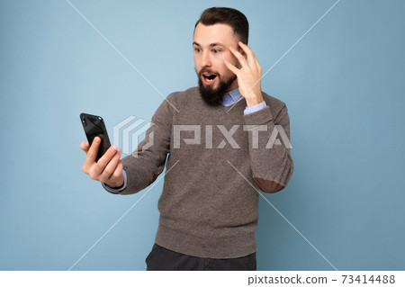 Photo of stunned amazed positive handsome young brunette unshaven man with beard wearing casual grey Photo of stunned amazed positive handsome young brunette unshaven man with beard wearing casual grey 73414488