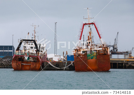 Red industrial trawler ships are moored in port 73414818