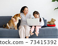 Asian mother and daughter sitting on sofa with their Shiba Inu and using laptop computer together. 73415392