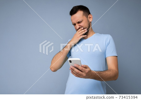 Photo of dissatisfied shocked handsome young man with beard wearing everyday blue t-shirt isolated 73415394
