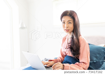 一個女人在床上拿電腦 73417182