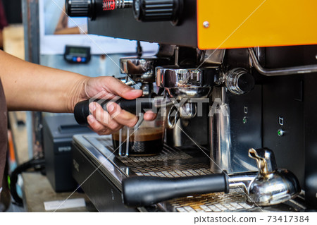 Espresso pouring machine with barista hand close up Espresso pouring machine with barista hand close up 73417384