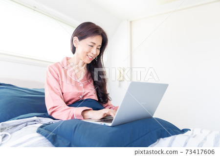 一個女人在床上拿電腦 73417606