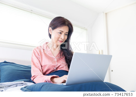 一個女人在床上拿電腦 73417653