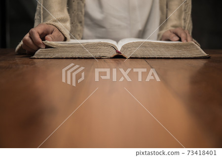 a woman reading a Bible on a wooden table. a woman reading a Bible on a wooden table. 73418401