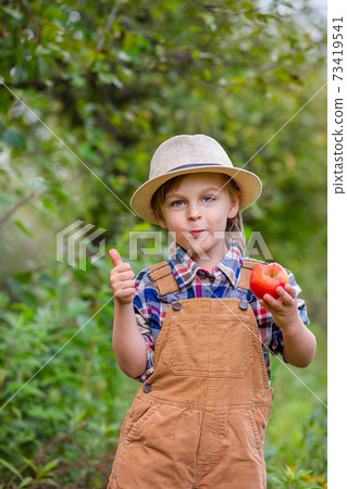 Portrait of one cute boy in a hat in the garden with a red apple, emotions, happiness, food. Autumn harvest of apples. Portrait of one cute boy in a hat in the garden with a red apple, emotions, happiness, food. Autumn harvest of apples. 73419541