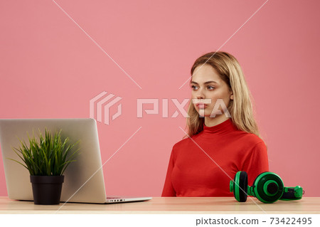 Woman sitting at a table in front of a laptop with a gamepad in hands playing technology headphones  73422495