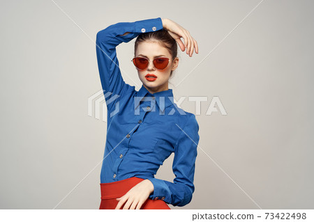 Fashionable woman in sunglasses and a blue shirt gesturing with her hands on a light background cropped view 73422498