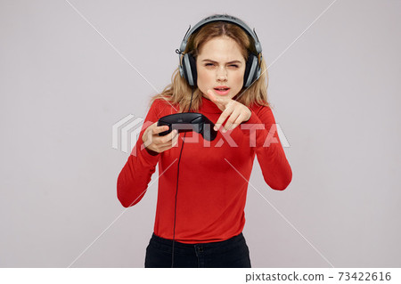 Woman with headphones Joystick in hands playing games fun leisure lifestyle entertainment red shirt gray background 73422616