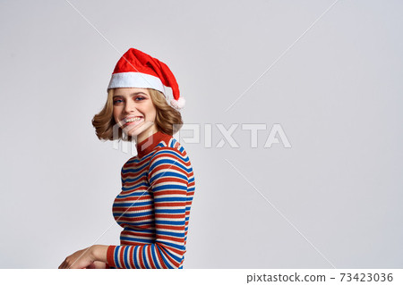 Happy woman in a Christmas cap and a striped sweater gestures with her hands for the New Year holidays 73423036