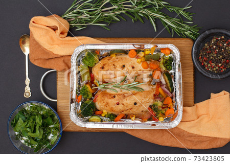 Baked chicken breasts or fillet in metal container with vegetables on cutting board and kitchen napkin. Baked chicken breasts or fillet in metal container with vegetables on cutting board and kitchen napkin. 73423805