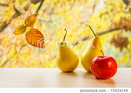 Apple, pears and autumn yellow leaf on window glass with water drops in the blurred background. 73424249