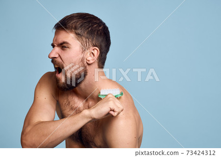 Man with naked shoulders body massager Skin care blue background Man with naked shoulders body massager Skin care blue background 73424312