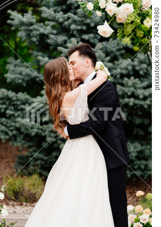 wedding ceremony in arch of living flowers.Beautiful newlyweds gently kissing wedding ceremony in arch of living flowers.Beautiful newlyweds gently kissing 73424980