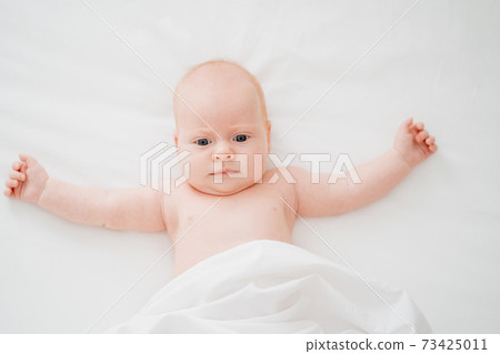 cute red-haired baby lies on a white bed. concept of baby care cute red-haired baby lies on a white bed. concept of baby care 73425011