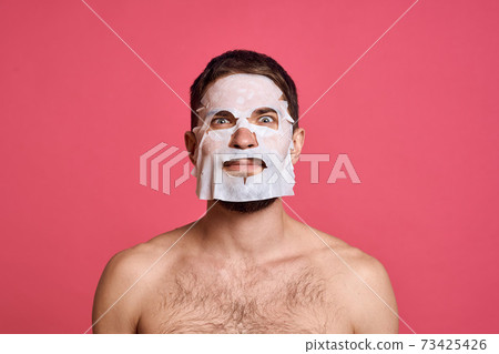 Man with bare shoulders in a white mask clear skin pink background Man with bare shoulders in a white mask clear skin pink background 73425426