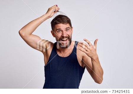 man with a massager for the head and in a blue t-shirt on a light background relaxing beard emotions 73425431