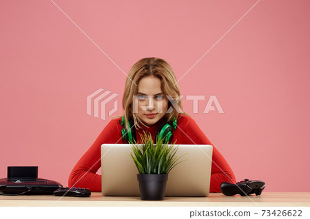 woman in headphones with gamepad in front of laptop sit at table entertainment lifestyle pink background woman in headphones with gamepad in front of laptop sit at table entertainment lifestyle pink background 73426622