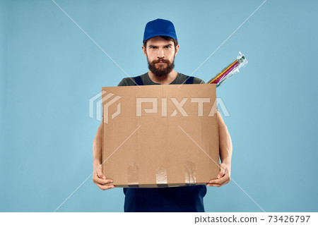 A man in working uniform with boxes in the hands of a carriage delivery service blue background 73426797