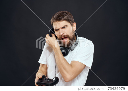 Man with joystick in hands headphones technology leisure game lifestyle dark isolated background Man with joystick in hands headphones technology leisure game lifestyle dark isolated background 73426979