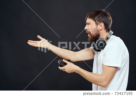 Man with joystick in hands headphones technology leisure game lifestyle dark isolated background Man with joystick in hands headphones technology leisure game lifestyle dark isolated background 73427195