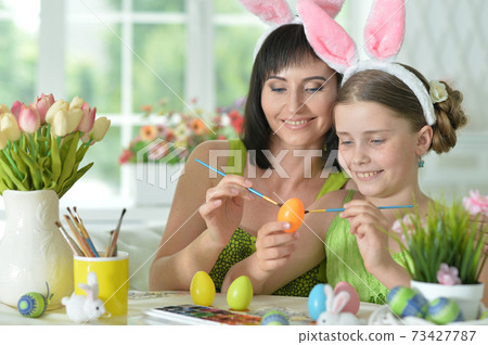 Mother with daughter wearing rabbit ears decorating Easter eggs Mother with daughter wearing rabbit ears decorating Easter eggs 73427787