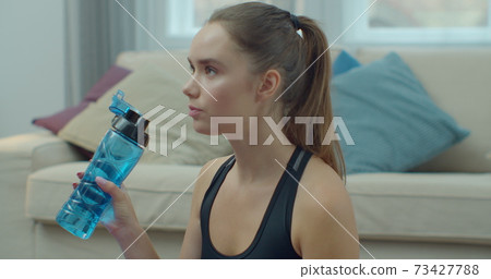 Beautiful woman drinking water and resting after training at home. Healthy lifestyle new normal quarantine during COVID or Corona virus pandemic concept. Beautiful woman drinking water and resting after training at home. Healthy lifestyle new normal quarantine during COVID or Corona virus pandemic concept. 73427788