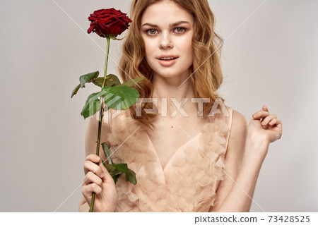 Portrait of a beautiful woman with a red rose on a beige background cropped view of an evening dress 73428525