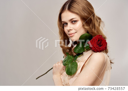 Portrait of a beautiful woman with a red rose on a beige background cropped view of an evening dress 73428557