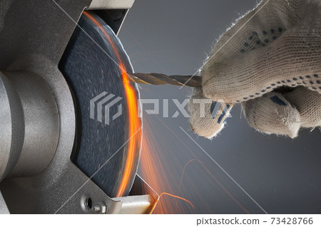 The hand wearing a work glove of man regrinding the drill tool for sharpen the drill tool with grinding wheel. The grinding wheel is hot and a lot of sparks. The hand wearing a work glove of man regrinding the drill tool for sharpen the drill tool with grinding wheel. The grinding wheel is hot and a lot of sparks. 73428766