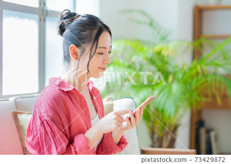 A woman who operates a smartphone while relaxing on the sofa. A woman who operates a smartphone while relaxing on the sofa. 73429872