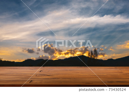 Empty space of plank wooden table, perspective view, blurred background of the mountainscape and wide blue sky at sunset, golden light and beautiful cloud. Blank tabletop for product display. 73430524