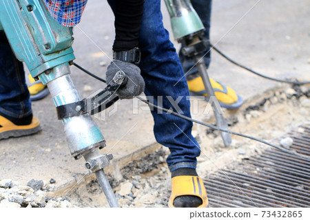 Male workers use electric concrete breaker for digging and drilling concrete repairing driveway surface with jackhammer at the local city road, during sidewalk, work construction site. Male workers use electric concrete breaker for digging and drilling concrete repairing driveway surface with jackhammer at the local city road, during sidewalk, work construction site. 73432865
