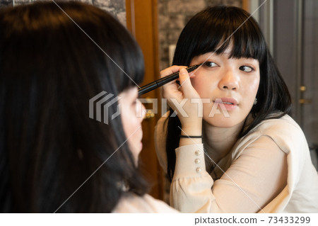 A woman who makes eye makeup through the mirror 73433299