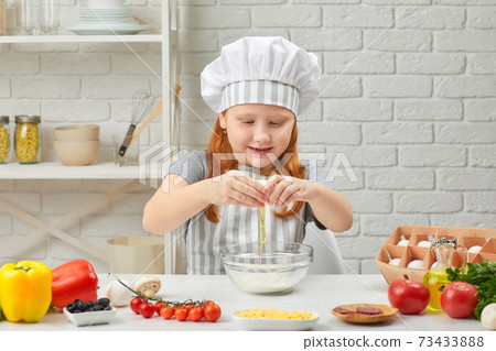 little girl is breaking yellow egg into fresh dough 73433888
